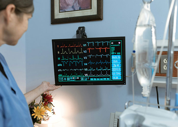 Medical professional examining an ECG monitor displaying heart rhythms and vital signs in a clinical setting.