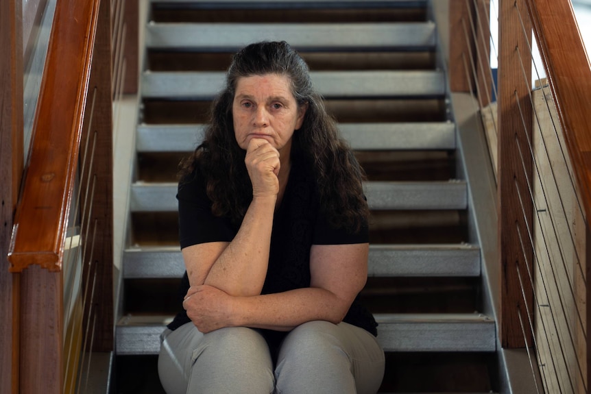 A woman sitting on stairs in a black shirt not smiling.