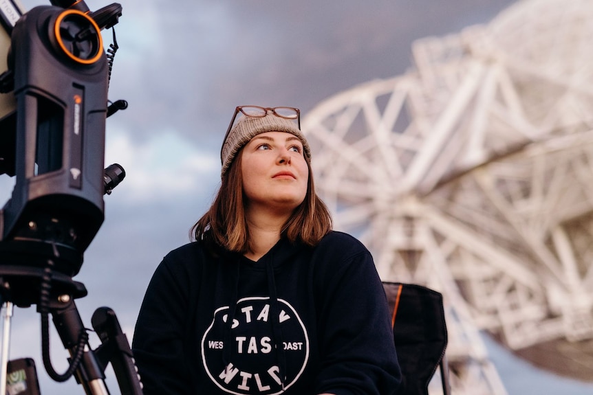 Woman with observation equipment in front of a radio telescope.