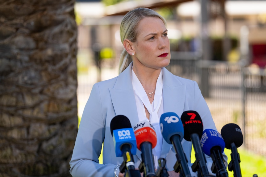 Ashton Hurn looks to the right of screen in front of six microphones