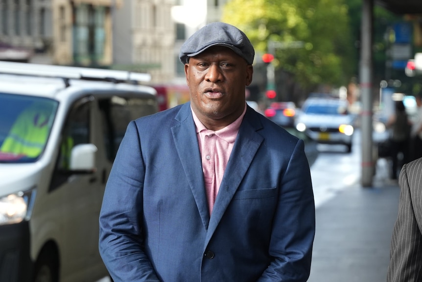 Man in dark suit, pink shirt and grey hat