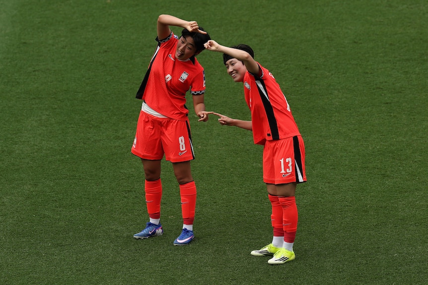 Two players from South Korea's women's football team form a love heart shape and smile for camera