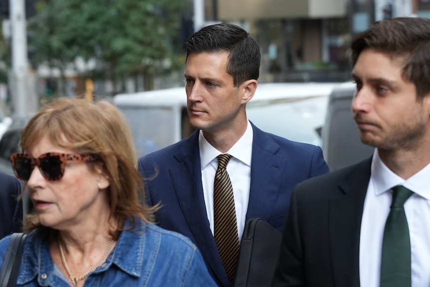 A man in a blue suit and brown tie leaves court with a group.
