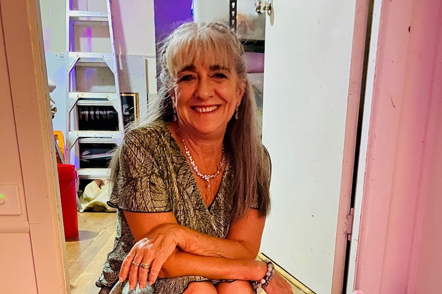 A woman wearing a glittering dress sits on the stairs grinning.