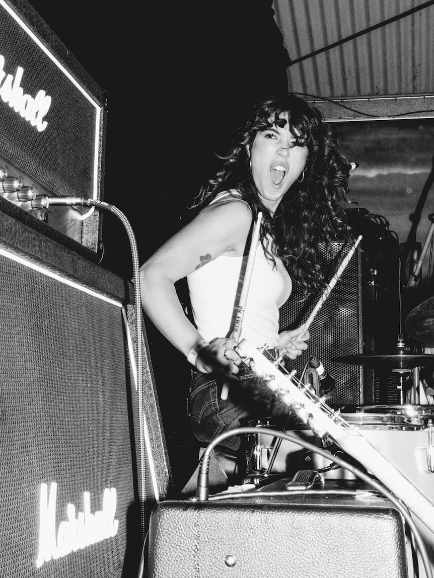 Black and white photo of woman on drums smiling while on stage