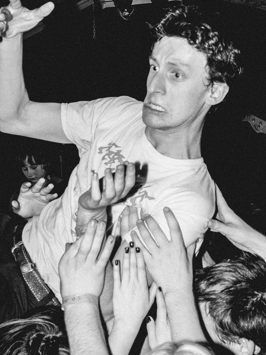 Black and white photo of a chaotic music event with a young man crowdsurfing across a lively crowd