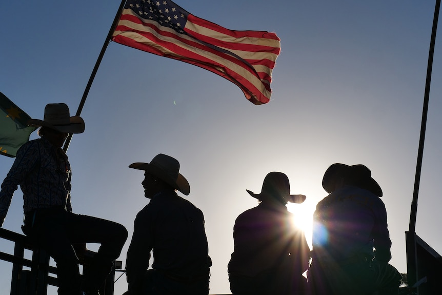 A backlit photo of people near a flag
