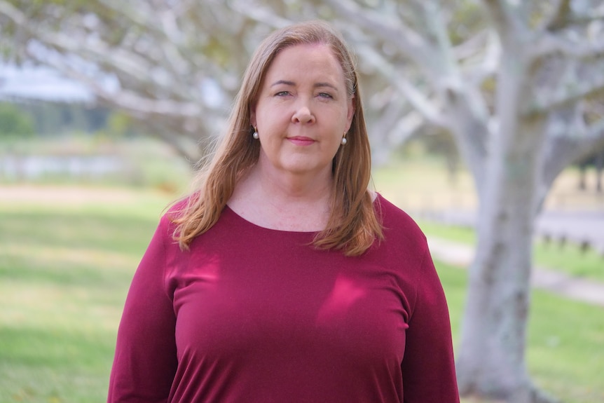 a woman standing in a park looking at the camera. She is not smiling