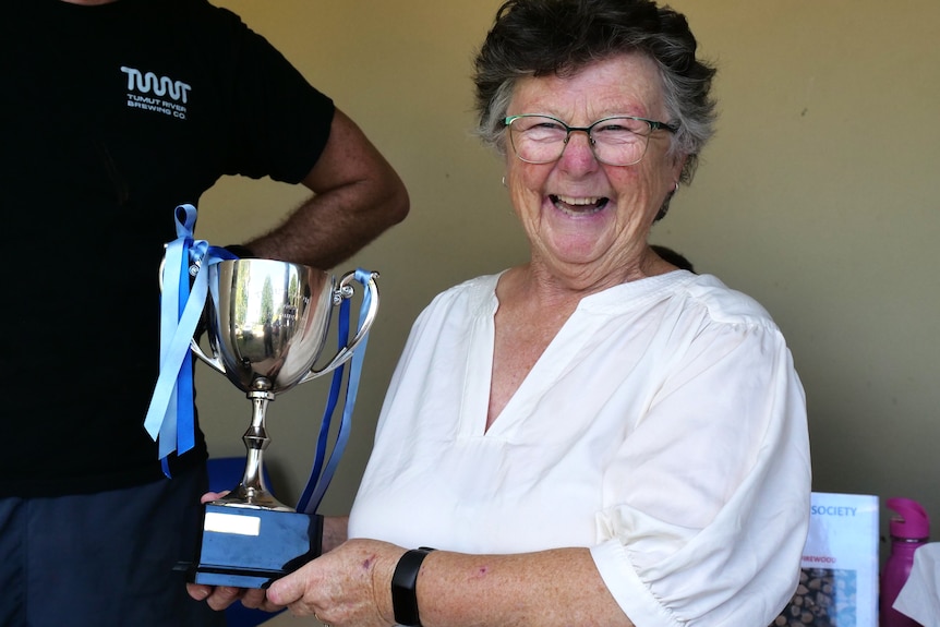 Woman in a white shirt holding a trophy shaped like a cup, smiling