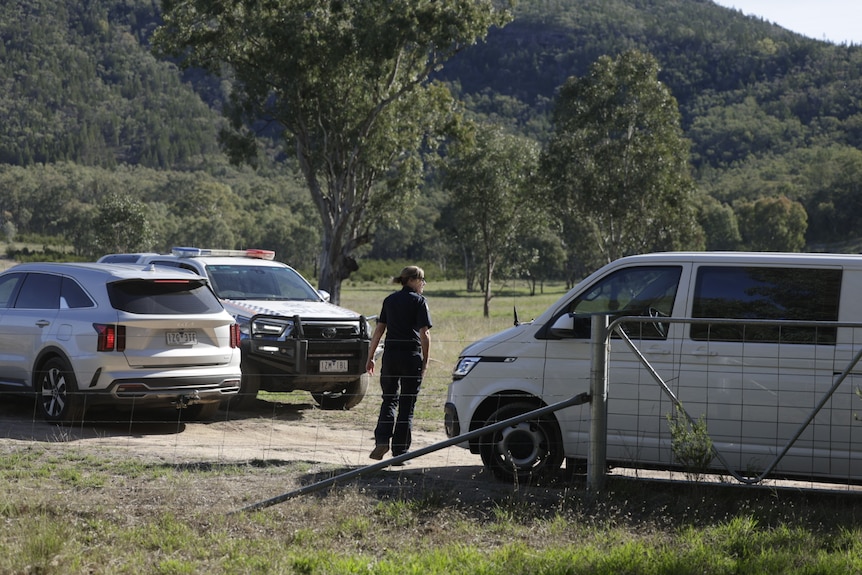 A police officer walks between three vehicles parked on a rural property.