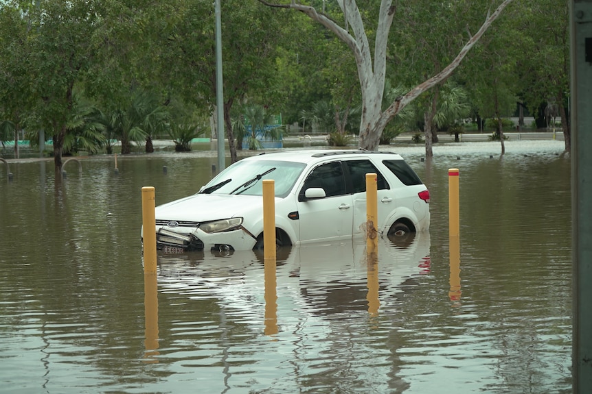 Floodwaters partially submerge an abandoned vehicle.
