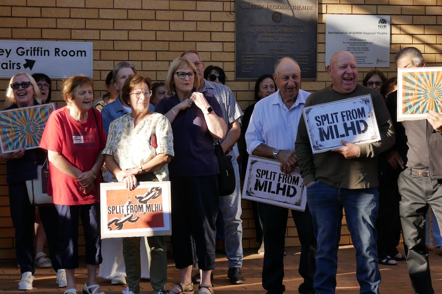 A group of men and women stand with placards calling for a health district split.