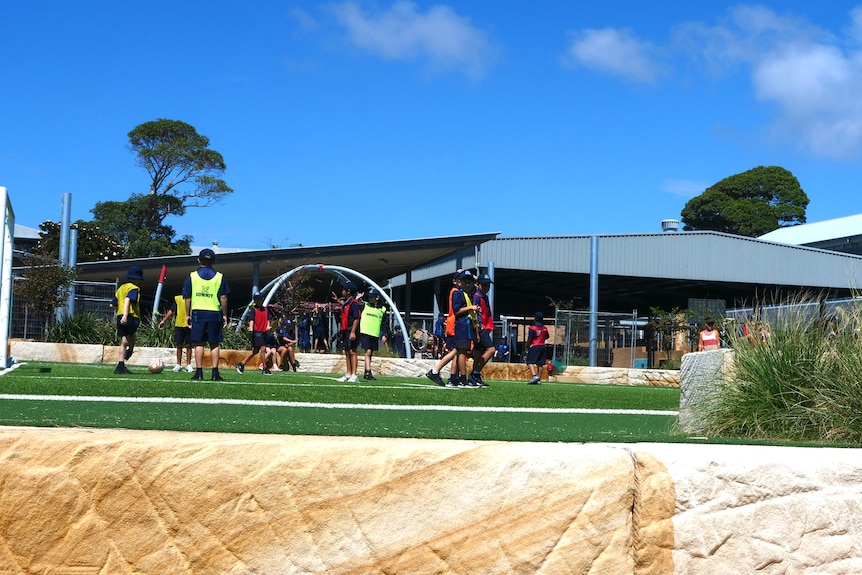 Students wearing fluorescent vests over their uniforms, playing soccer.