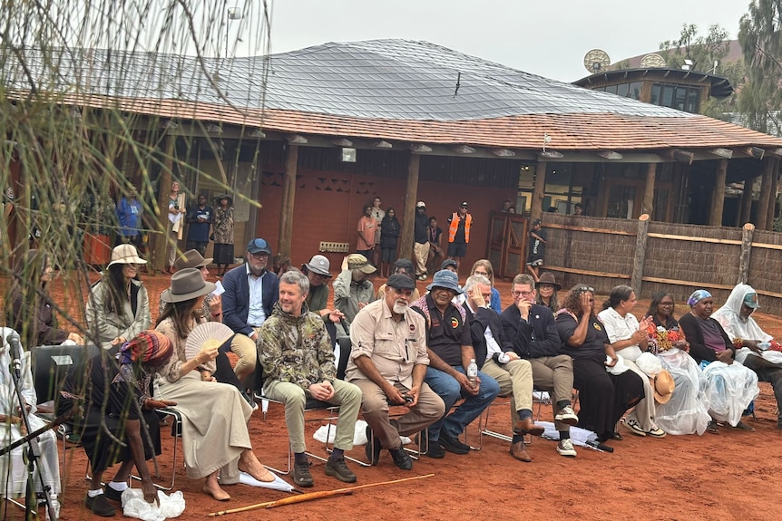 A crowd of people sit on chairs outside a building in the outback.