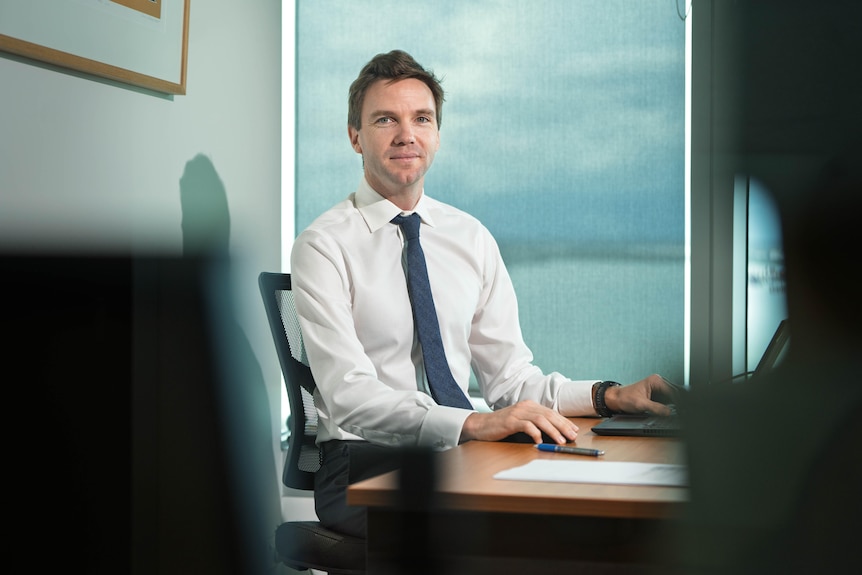 A man in a white shirt and blue tie sits at a desk