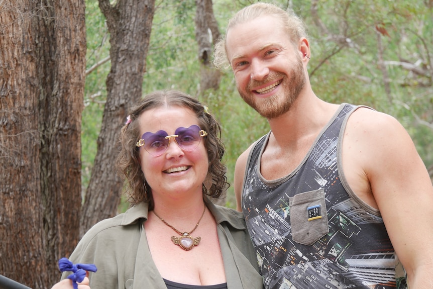 A woman wearing purple glasses smiling standing next to a blonde smiling man.