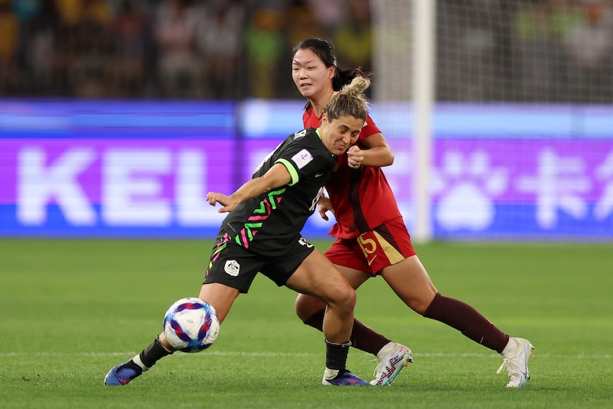 Two soccer players, one in blue and one in red, tussle for the ball