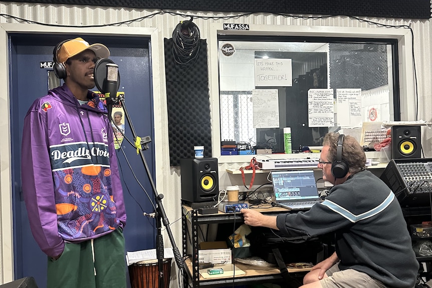an artist singing in a recording studio while a music producer controls sound equipment