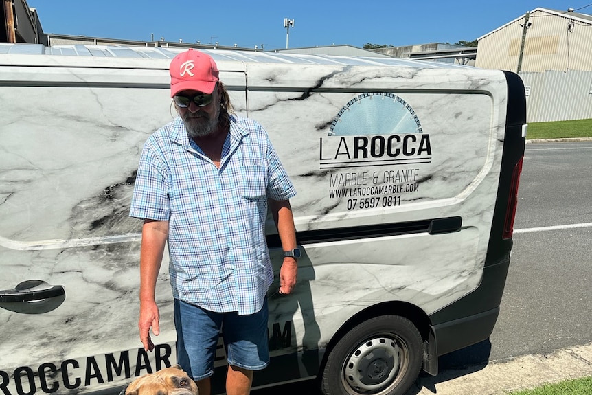 A man named Derick standing next to his work van with his dog sitting on the ground