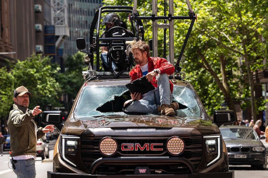 David Leitch talks to Ryan Gosling who is sitting on a car onthe set in sydney for the film the fall guy