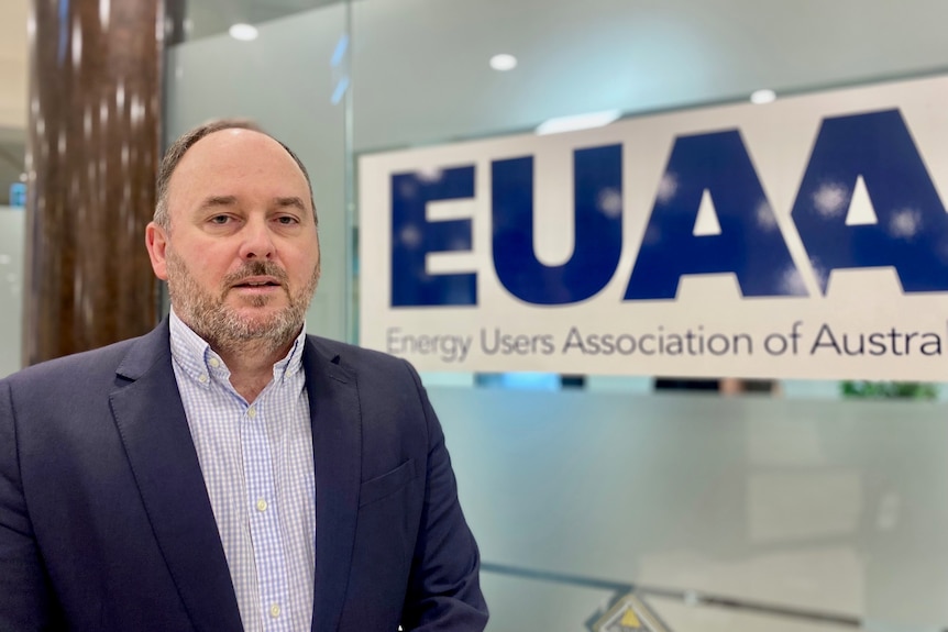 A middle aged man in a suit stands in front of his office door.