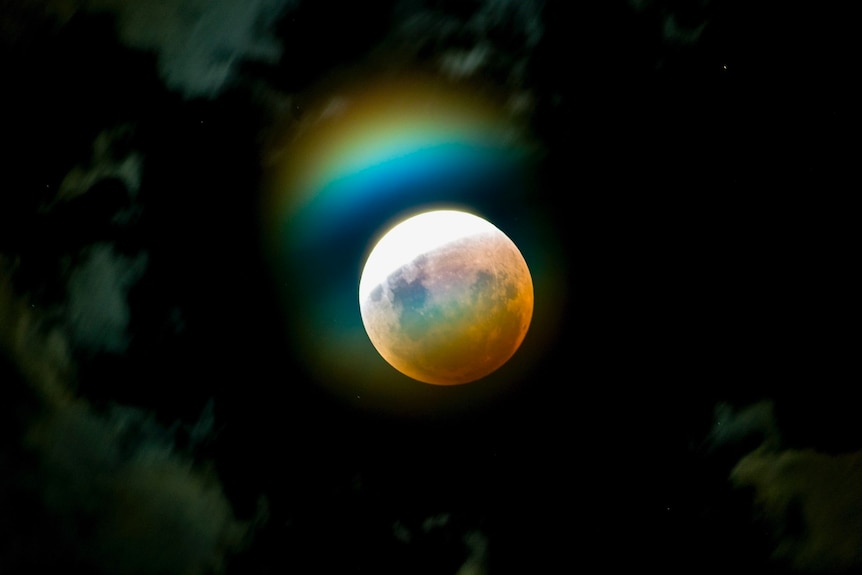 A half red, half white moon with a rainbow reflection above it in a dark sky