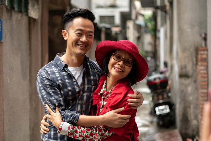 Jenny Law, dressed in bright red, smiles while hugging her son, Benjamin Law, in a laneway