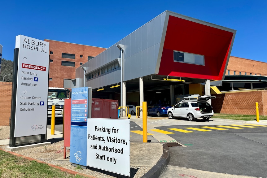 A front view of the Albury Wodonga hospital, a sign directs to the emergency department, car park and cancer centre.