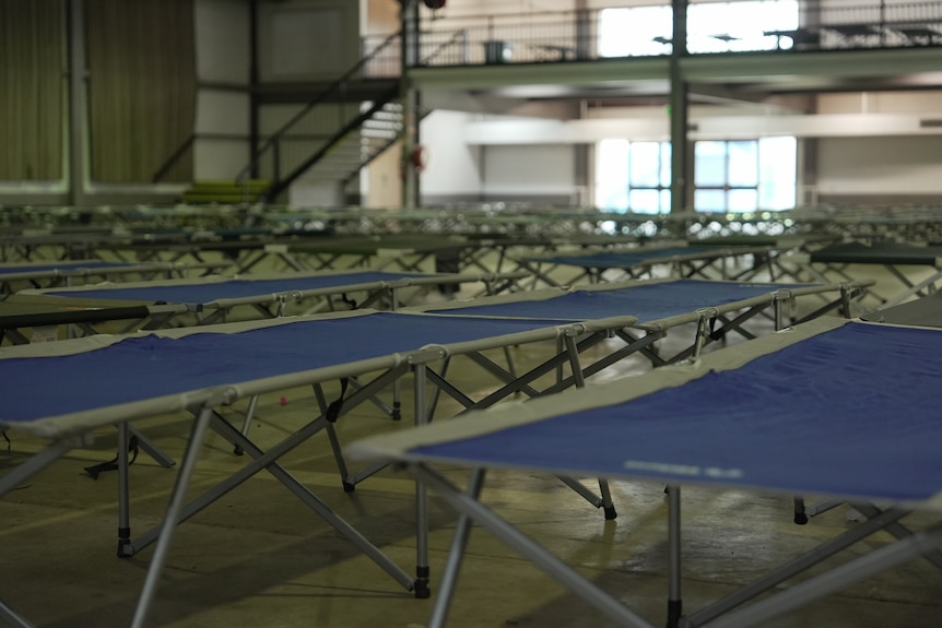 Rows of camping beds set up inside a large hall.