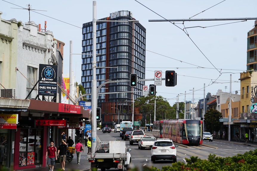 A large apartment building on a busy road with cars and a light rail vehicle on it.