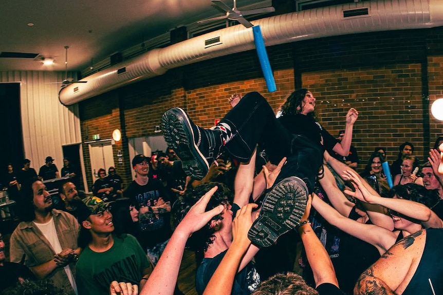 A person crowdsurfing on their back as the crowd holds them up.