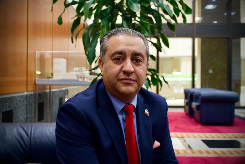 A middle-aged man in a dark suit sits in a lounge area in a corporate building.