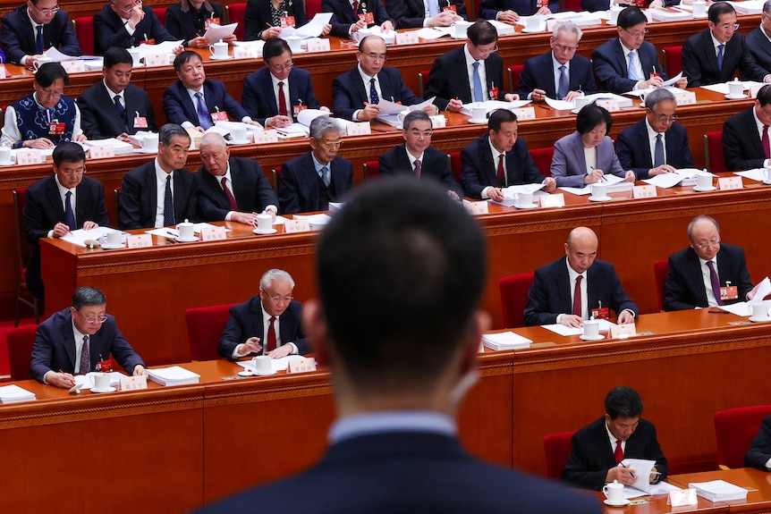 Men sitting in pews look on at the red Great Hall.