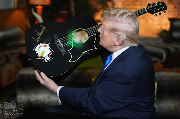Donald Trump holds up replica of an Elvis Presley guitar after signing it.