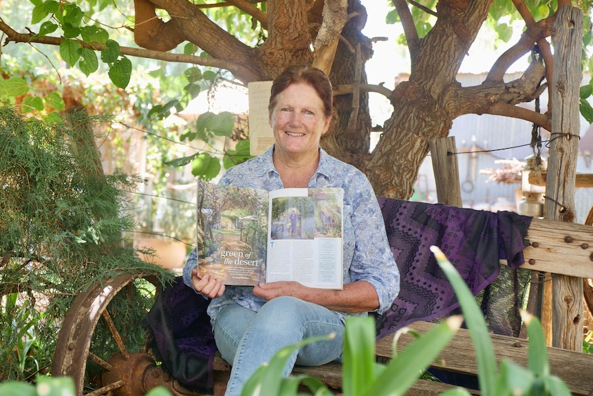 A woman with red hair sits on a bench holding a magazine.