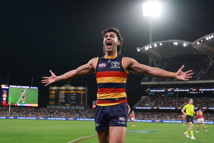 Adelaide AFL player Josh Rachele stands on the boundary with arms spread in celebration after kicking a key goal.