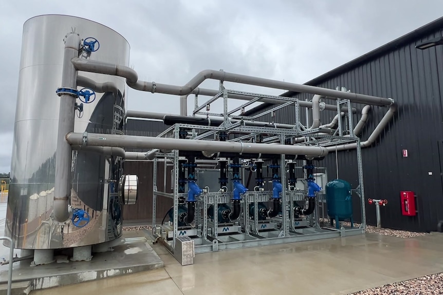 A large stainless steel vat connected to pipes with wheels on them. its a water recycling system at a factory.
