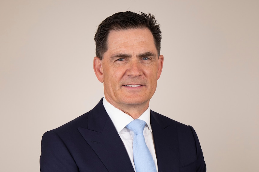 Marcus Padley headshot in a suit, Caucasian, dark hair, light blue tie.