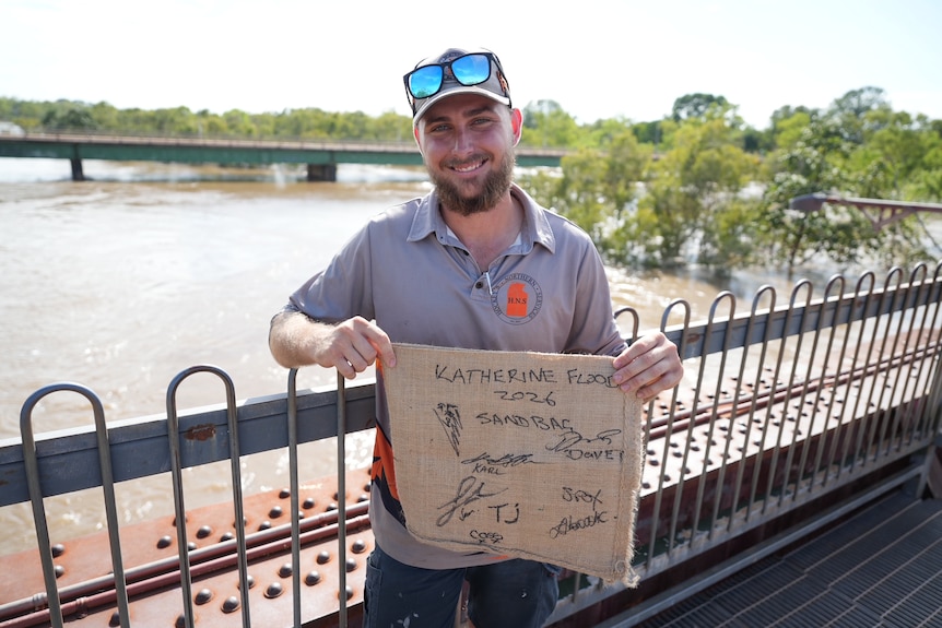 A man holds a signed sandbag on the bridge over the swollen Katherine River