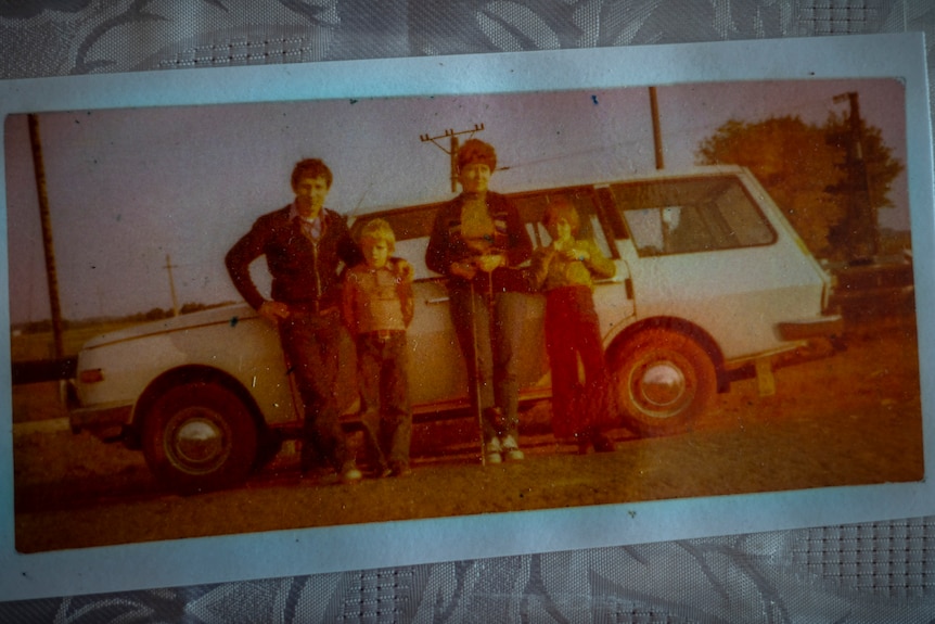 Old photograph of parents and two young boys standing in front of a white station wagon