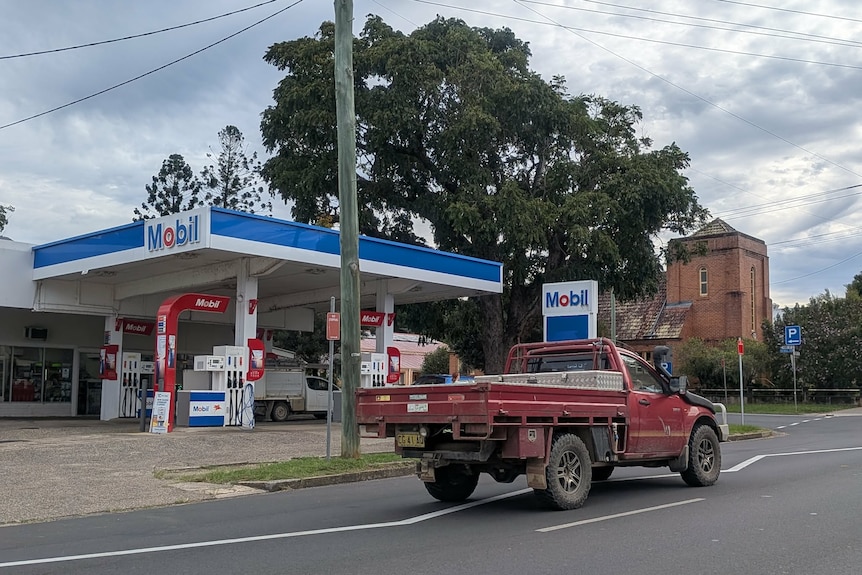 Ute drives past Bellingen Mobil service station with large tree and church behind