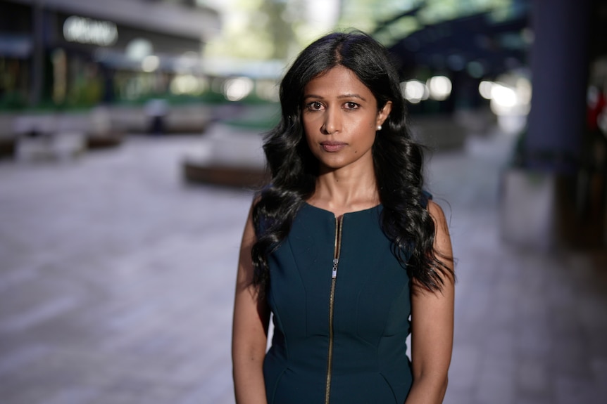 Pramudie Gunaratne, wearing a dark dress, looks at the camera with a sombre expression.