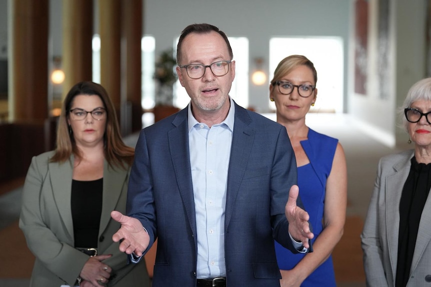 David Shoebridge stands with his hands open flanked by his Greens colleagues.