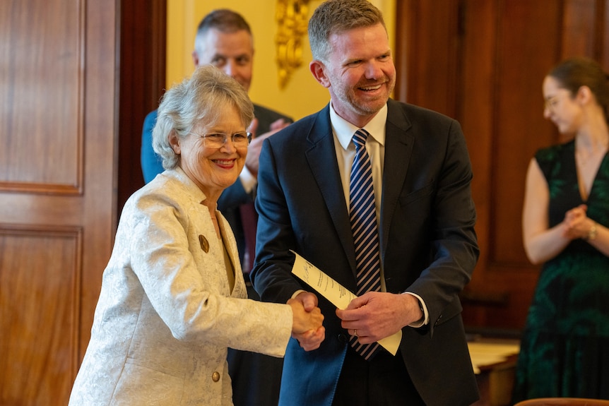 A woman shakes a man's hand and looks towards a crowd.