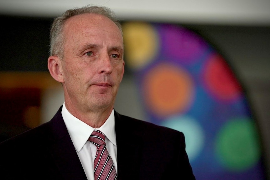A man in a suit and tie against a colourful background.