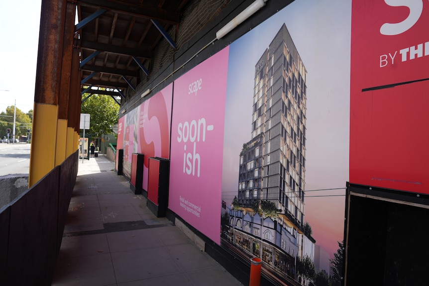 A long billboard-like sign featuring a Scape apartment placed under scaffolding of the building in progress.