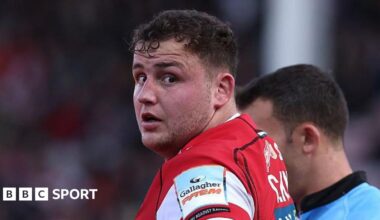 Gloucester prop Ciaran Knight in a cherry and white shirt looks towards the camera, with a blue-shirted referee standing just behind him.
