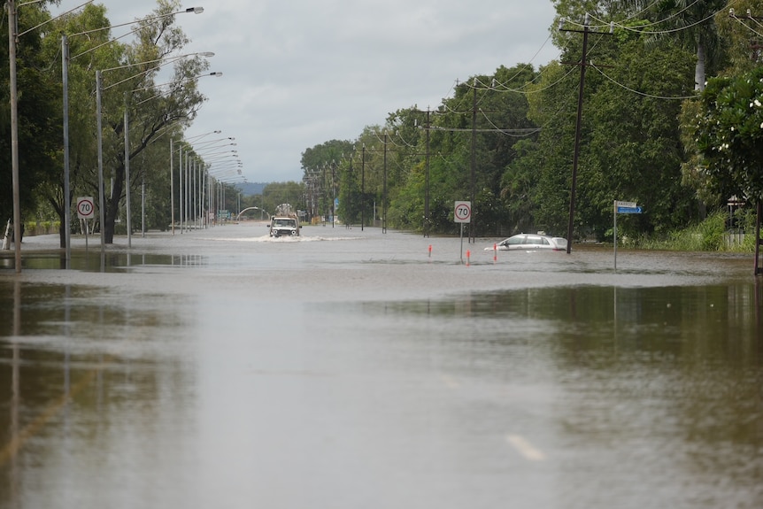 A vehicle driving slowly over a flooded road.