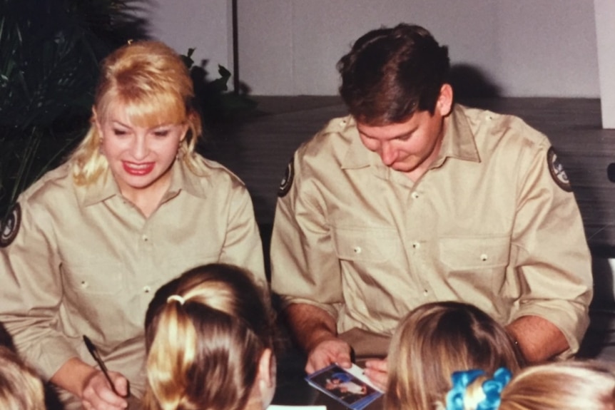 A woman and a man in ranger uniforms signing autographs for a crowd of children.