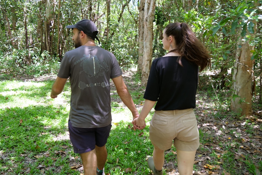 Kyla and Jason holding hands walking in rainforest, their backs to the camera.